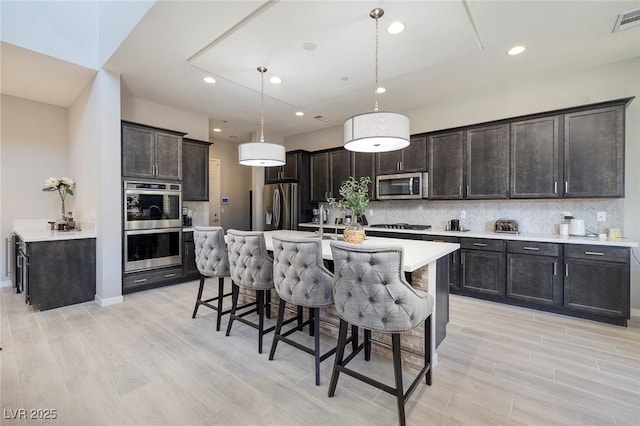 kitchen featuring pendant lighting, stainless steel appliances, a kitchen island with sink, and dark brown cabinets