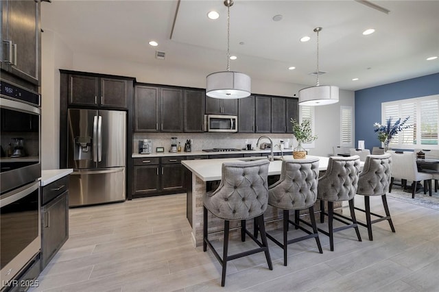 kitchen featuring appliances with stainless steel finishes, a kitchen bar, decorative backsplash, hanging light fixtures, and a kitchen island with sink