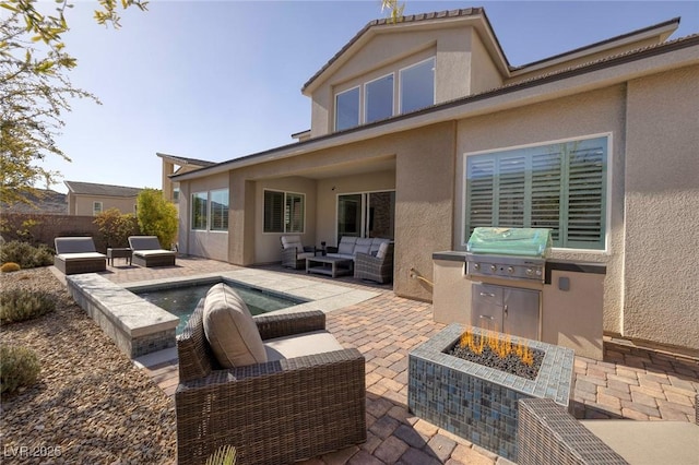 back of house with an outdoor kitchen, a patio, and an outdoor living space with a fire pit