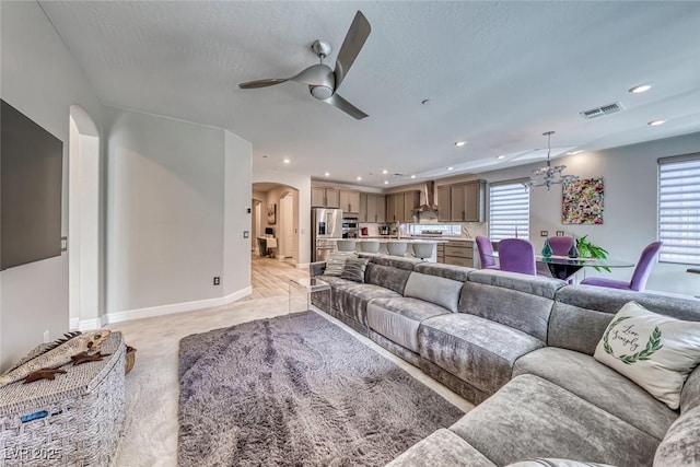 carpeted living room with ceiling fan with notable chandelier and a textured ceiling