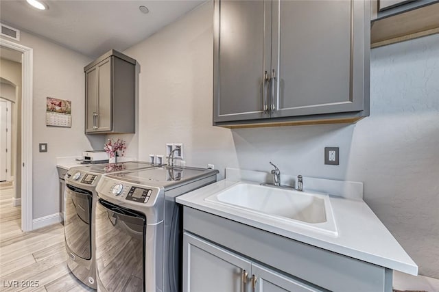 clothes washing area featuring sink, light hardwood / wood-style flooring, cabinets, and washing machine and clothes dryer