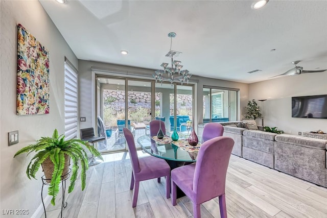 dining room with plenty of natural light, ceiling fan with notable chandelier, and light wood-type flooring