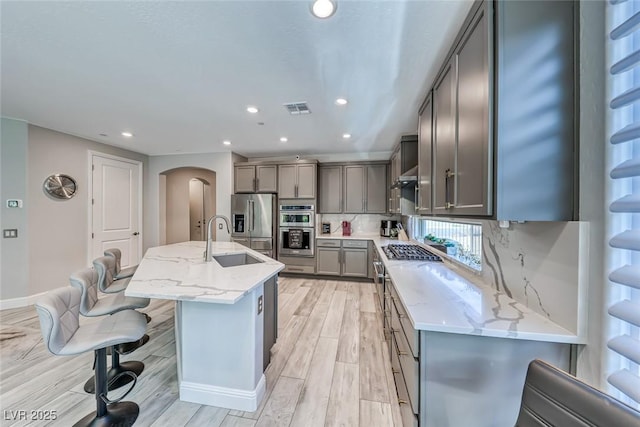 kitchen with sink, light stone counters, appliances with stainless steel finishes, a kitchen island with sink, and decorative backsplash