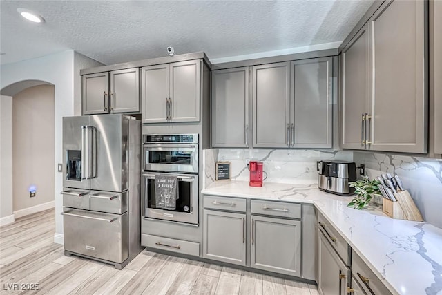 kitchen with appliances with stainless steel finishes, gray cabinetry, light stone counters, and decorative backsplash