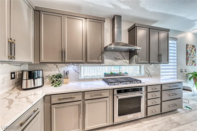 kitchen with backsplash, appliances with stainless steel finishes, gray cabinets, and wall chimney range hood