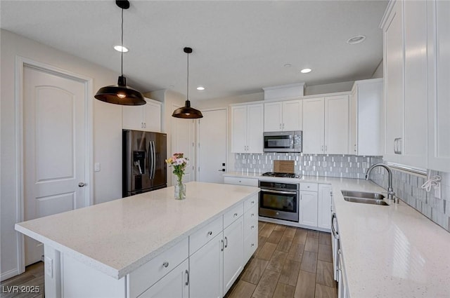 kitchen with sink, appliances with stainless steel finishes, hanging light fixtures, white cabinets, and a kitchen island