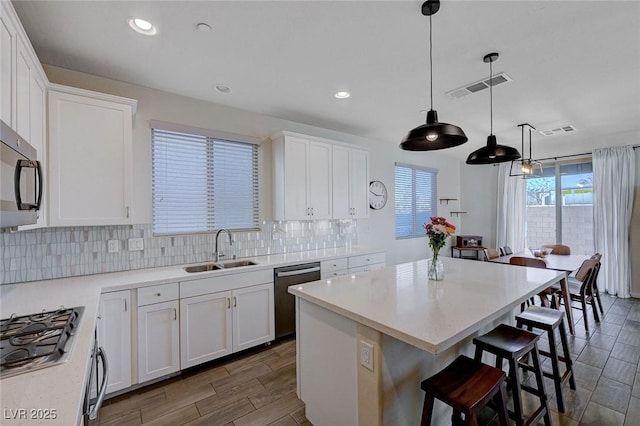 kitchen featuring pendant lighting, sink, white cabinetry, stainless steel appliances, and a center island