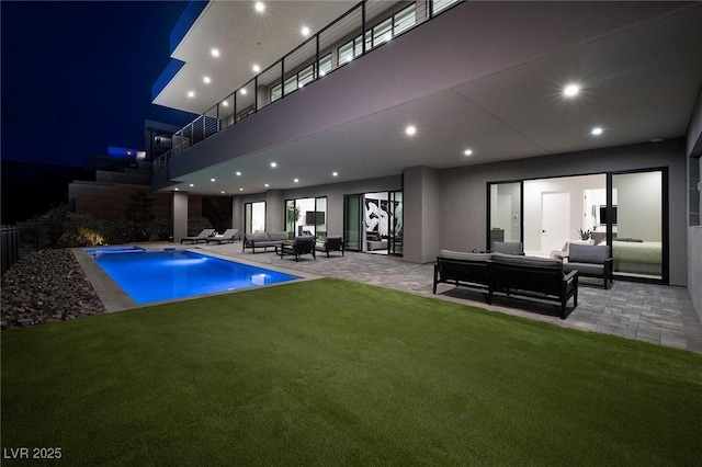 pool at night with an outdoor hangout area, a patio, and a lawn