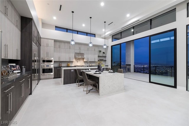 kitchen featuring a breakfast bar, a high ceiling, a kitchen island, decorative light fixtures, and stainless steel oven