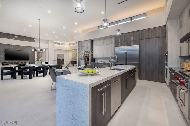 kitchen with sink, decorative light fixtures, light tile patterned floors, appliances with stainless steel finishes, and a kitchen island with sink