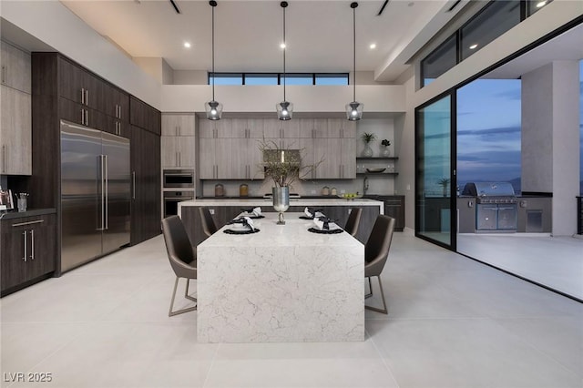 kitchen featuring stainless steel built in refrigerator, a breakfast bar, a kitchen island with sink, and decorative light fixtures