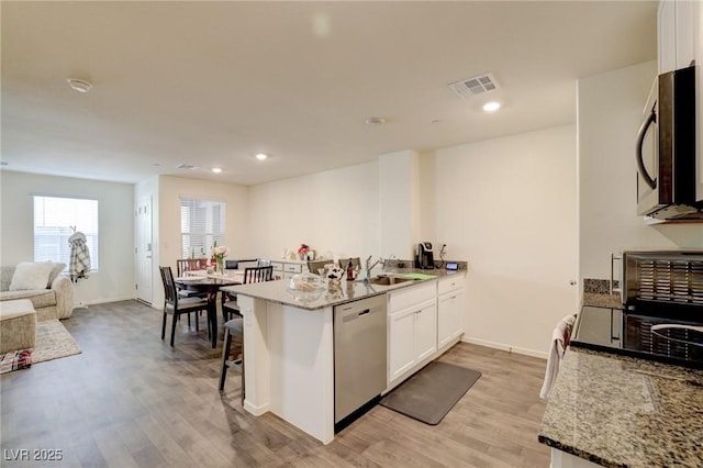 kitchen with a kitchen breakfast bar, light stone countertops, stainless steel dishwasher, light hardwood / wood-style floors, and white cabinetry