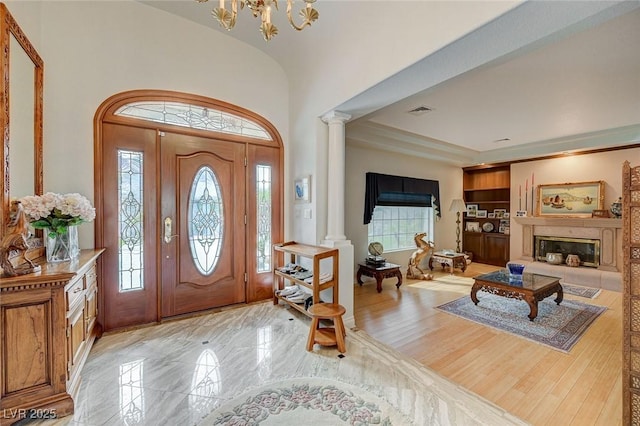 foyer entrance with ornate columns, light hardwood / wood-style flooring, a raised ceiling, a notable chandelier, and a premium fireplace