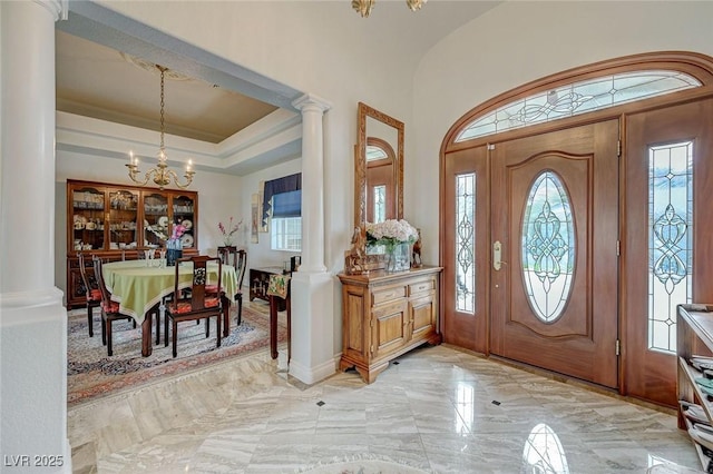 foyer with an inviting chandelier, a raised ceiling, and ornate columns