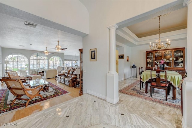 interior space featuring decorative columns, ceiling fan with notable chandelier, a textured ceiling, and a tray ceiling