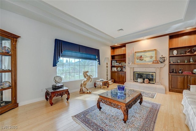 living room with hardwood / wood-style floors, built in features, and a raised ceiling