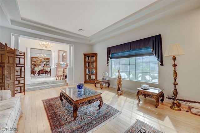 living area featuring an inviting chandelier, hardwood / wood-style flooring, a raised ceiling, and ornate columns