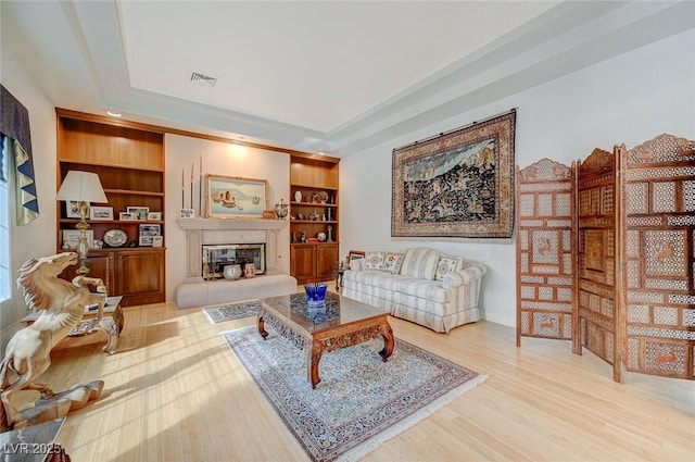 living room featuring a tray ceiling, built in features, a premium fireplace, and hardwood / wood-style flooring