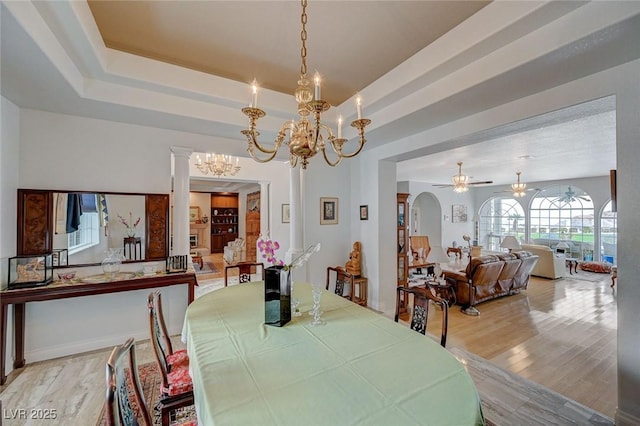 dining area featuring ceiling fan with notable chandelier, light hardwood / wood-style flooring, and a raised ceiling