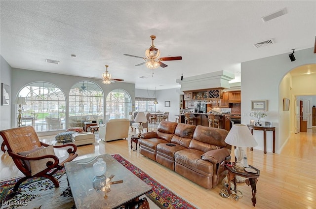 living room with ceiling fan, a healthy amount of sunlight, a textured ceiling, and light hardwood / wood-style flooring