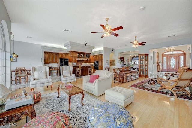 living room with ceiling fan with notable chandelier and light hardwood / wood-style flooring