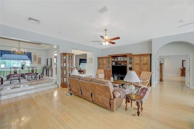 living room featuring a tray ceiling, ceiling fan with notable chandelier, and light wood-type flooring