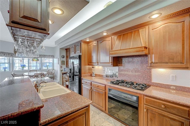 kitchen featuring premium range hood, tasteful backsplash, sink, black appliances, and light stone countertops