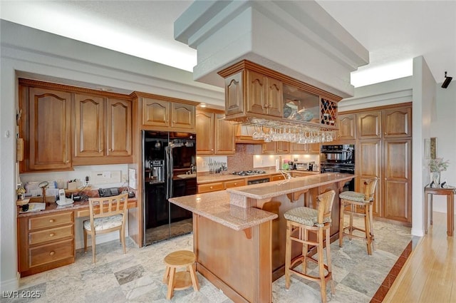 kitchen with an island with sink, a kitchen breakfast bar, decorative backsplash, black appliances, and light stone countertops