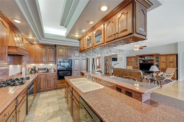 kitchen with sink, ceiling fan, light stone counters, black appliances, and a raised ceiling