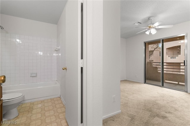 bathroom with ceiling fan, a textured ceiling, toilet, and tiled shower / bath