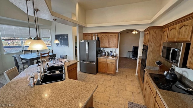 kitchen featuring pendant lighting, sink, a high ceiling, black appliances, and an island with sink