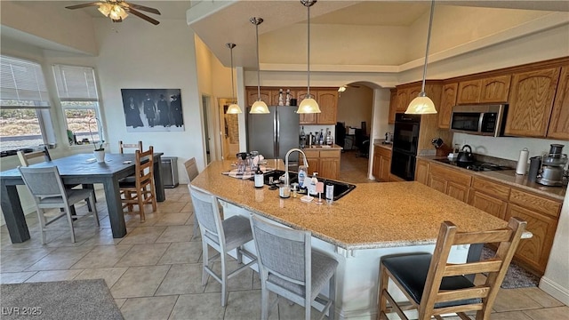 kitchen with decorative light fixtures, a kitchen island with sink, sink, and black appliances