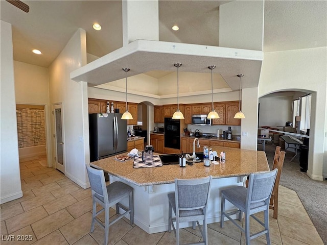 kitchen with a kitchen breakfast bar, a high ceiling, hanging light fixtures, a kitchen island with sink, and stainless steel appliances