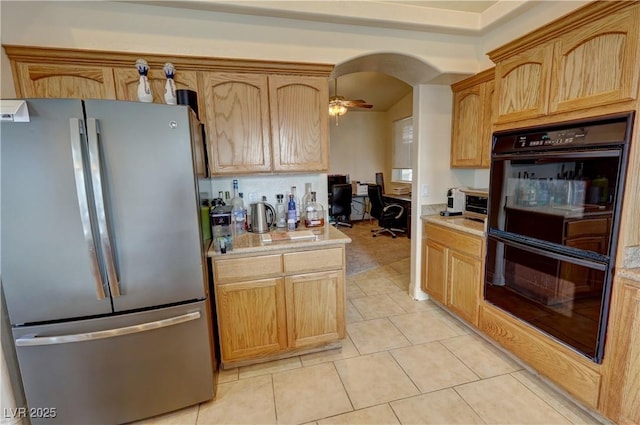 kitchen with light brown cabinetry, stainless steel refrigerator, double oven, light tile patterned floors, and ceiling fan