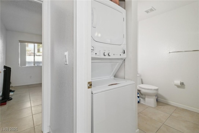 laundry area with light tile patterned flooring and stacked washing maching and dryer