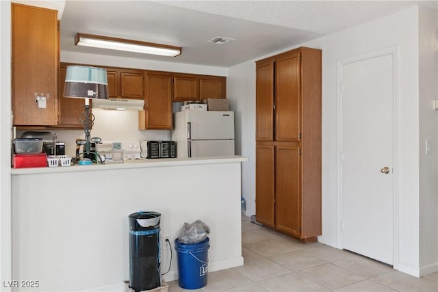 kitchen featuring range, kitchen peninsula, white fridge, and light tile patterned floors