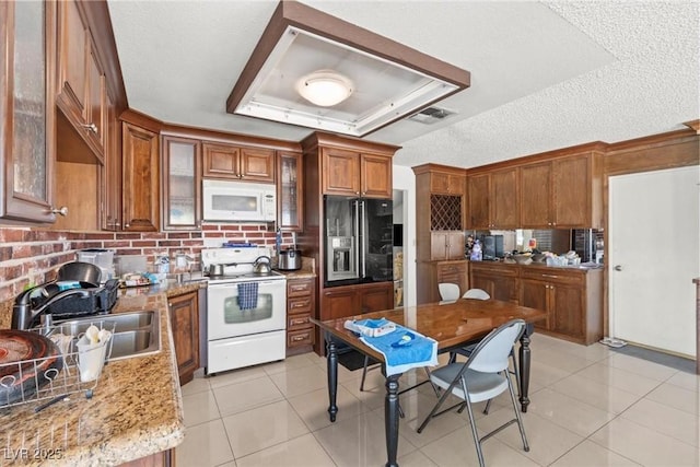 kitchen with visible vents, brown cabinets, light tile patterned flooring, white appliances, and a sink