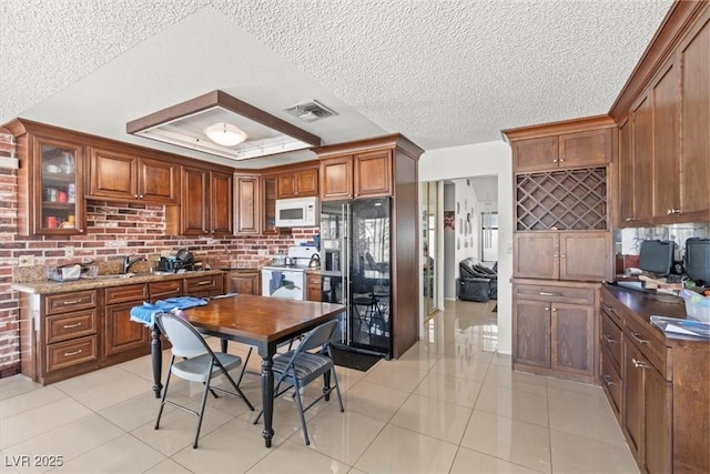 kitchen featuring visible vents, brown cabinets, white appliances, light tile patterned flooring, and a raised ceiling