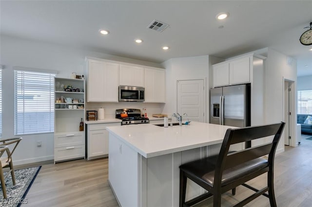 kitchen with white cabinetry, a kitchen island with sink, stainless steel appliances, and light hardwood / wood-style flooring