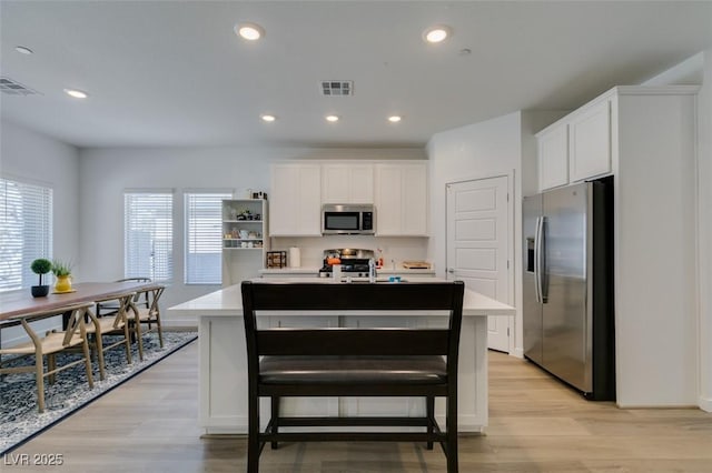 kitchen with white cabinetry, appliances with stainless steel finishes, light hardwood / wood-style floors, and a center island with sink