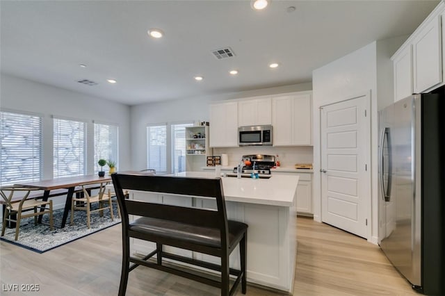 kitchen with light wood-type flooring, stainless steel appliances, a kitchen island with sink, and white cabinets