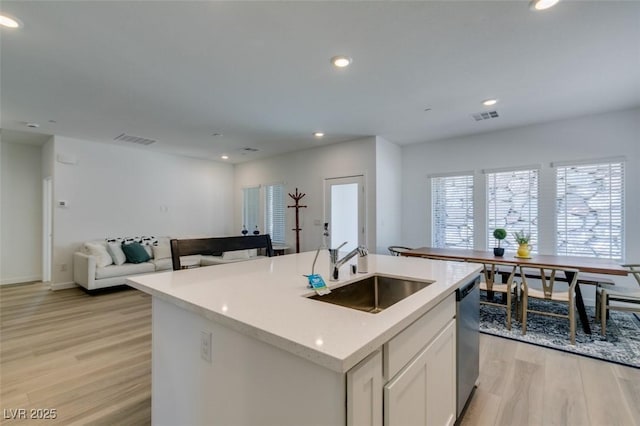 kitchen with sink, white cabinetry, light wood-type flooring, dishwasher, and a kitchen island with sink