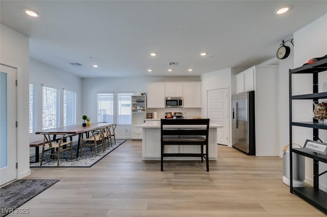 kitchen featuring appliances with stainless steel finishes, a kitchen island, white cabinets, a kitchen bar, and light wood-type flooring