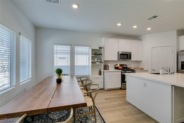 kitchen with sink, light wood-type flooring, white cabinets, and appliances with stainless steel finishes