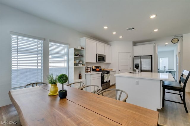 kitchen with white cabinetry, appliances with stainless steel finishes, a breakfast bar, and a kitchen island with sink