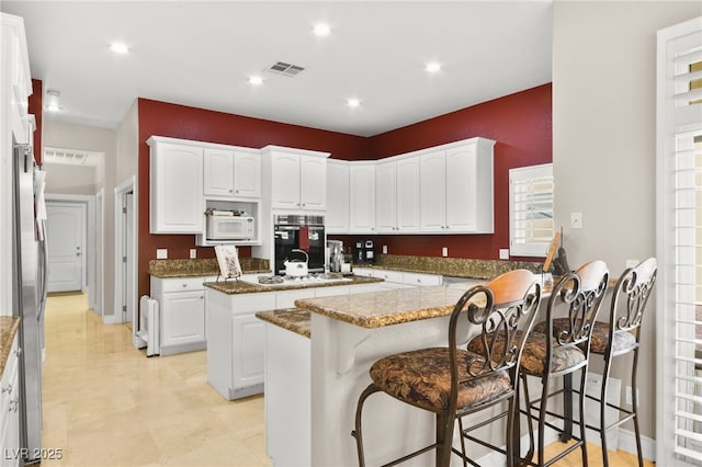 kitchen with white cabinetry, white appliances, a kitchen island, and stone counters