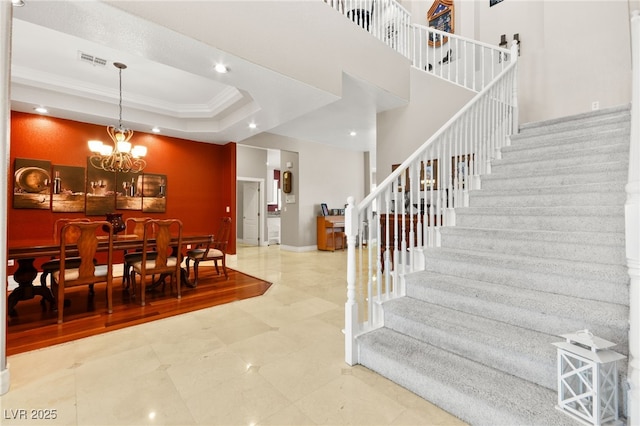 interior space with an inviting chandelier, a towering ceiling, ornamental molding, and a raised ceiling