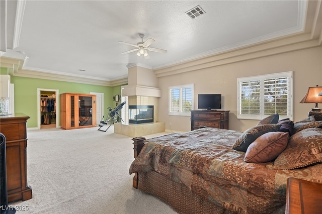 carpeted bedroom with crown molding, ceiling fan, a spacious closet, and a tile fireplace