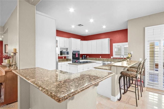 kitchen featuring a breakfast bar area, appliances with stainless steel finishes, kitchen peninsula, light stone countertops, and white cabinets