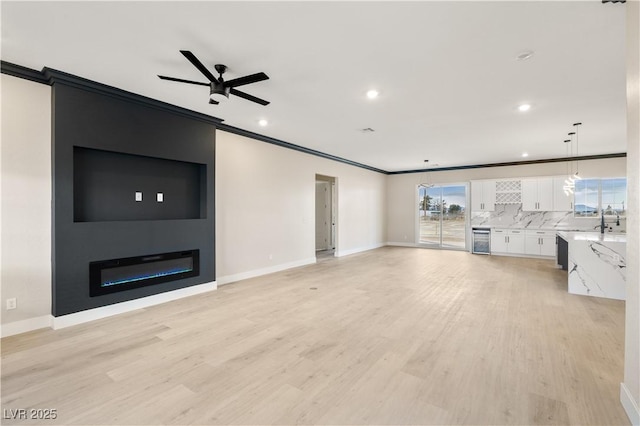 unfurnished living room with sink, light hardwood / wood-style flooring, a large fireplace, ornamental molding, and ceiling fan